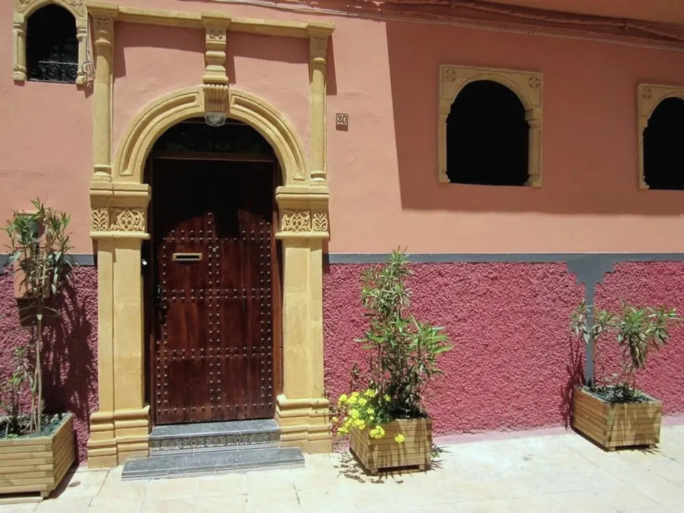 The pink façade of Dar Yanis: a studded cedar door in a carved Salé-stone arch, with plants in wooden planters